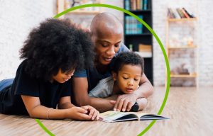 A father laying on the ground with his two children while reading a book 